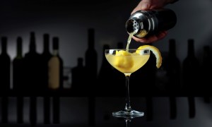 Cocktail "Sidecar" on a black reflective background. The bartender pours a cocktail from a shaker into a glass with ice