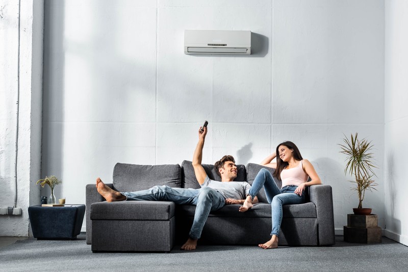 boyfriend switching on air conditioner and looking at smiling girlfriend