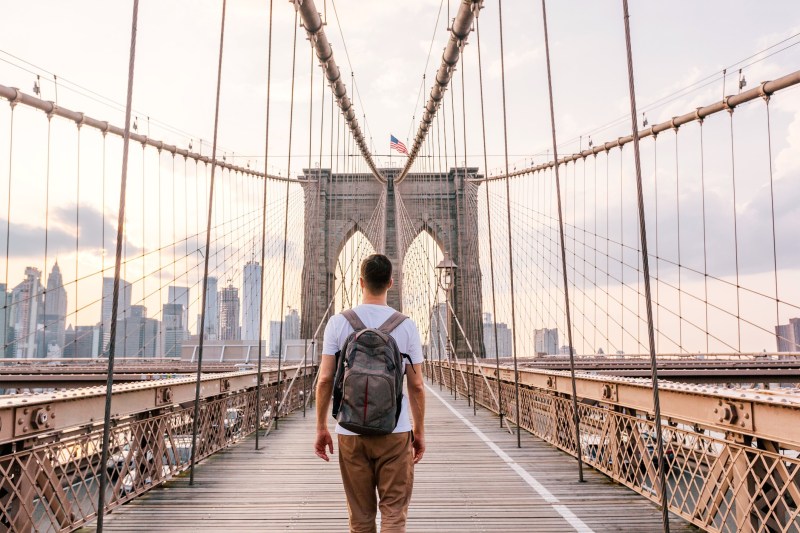 Rear view of a young man with backpack walking on Brooklyn Bridge, New York City, USA
