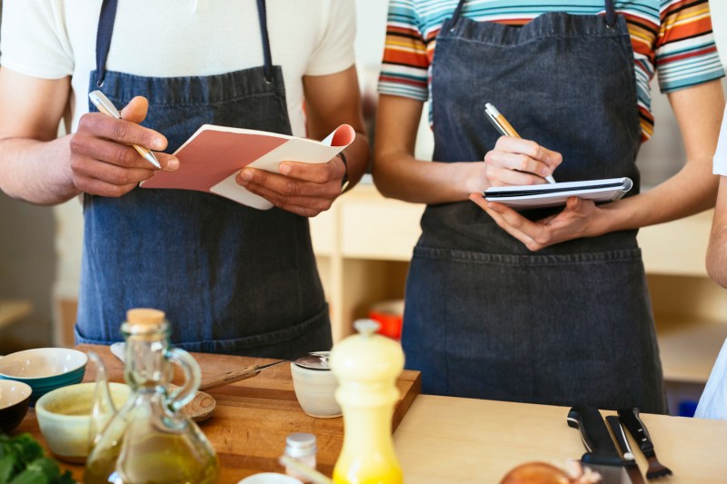 A close-up of a man and woman taking notes during a cooking class.
