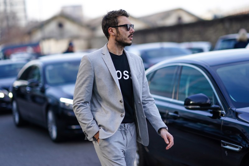 A man wearing a blazer, a Boss pullover, and sunglasses. 
