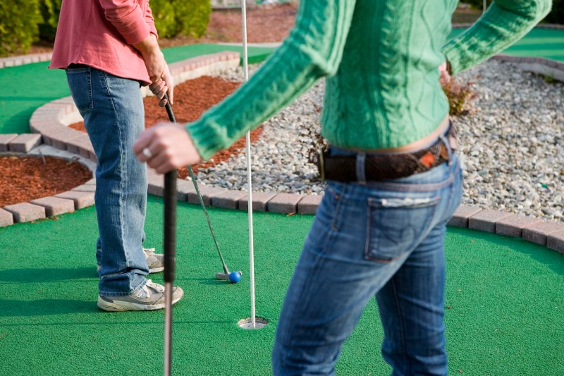 A lower body shot of a couple playing mini golf.