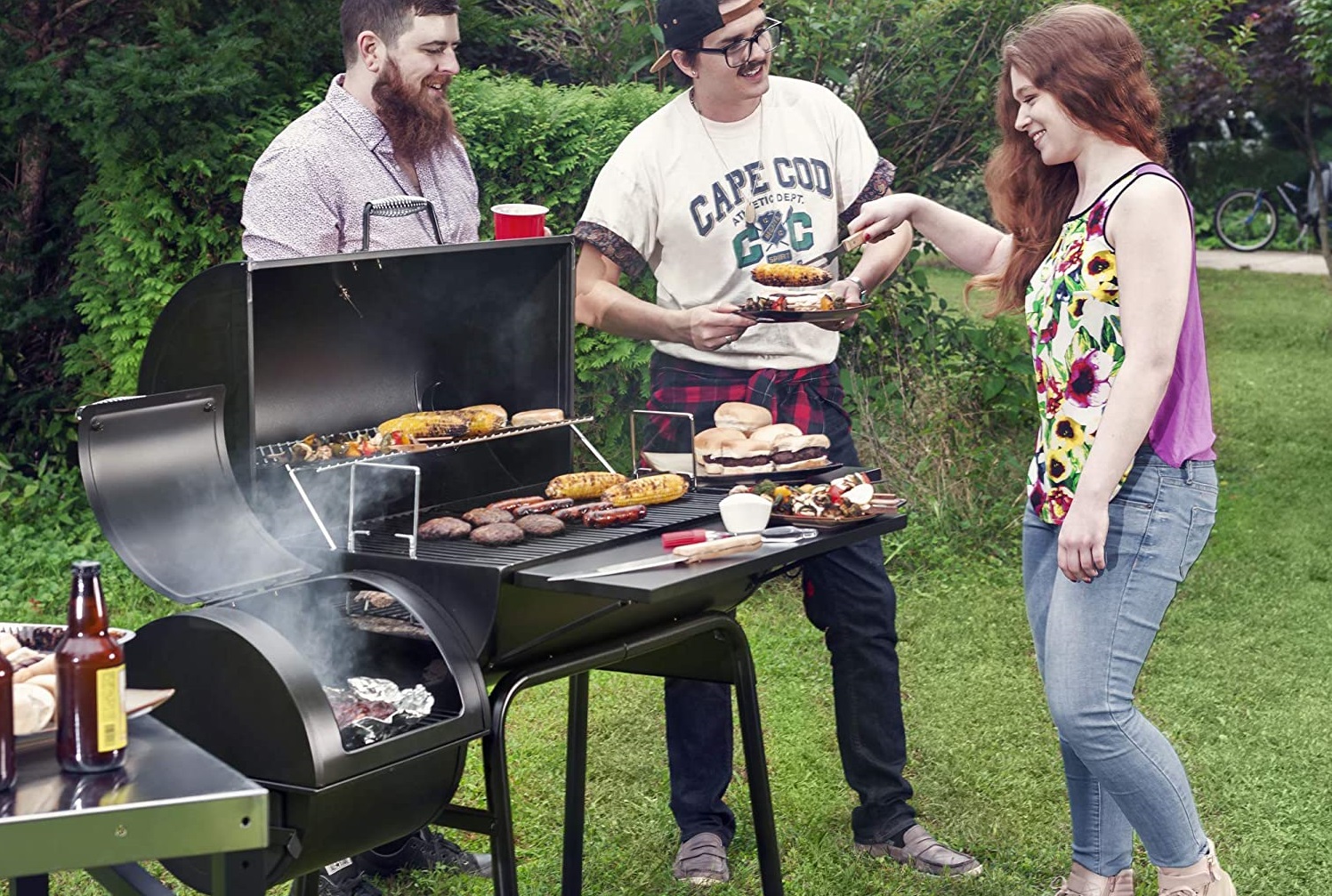 Two men and a woman grilling burgers and corn on a Royal Gourmet Charcoal Grill with Offset Smoker.