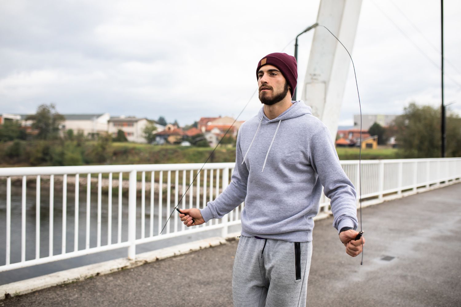 A bearded man skipping rope on a bridge.