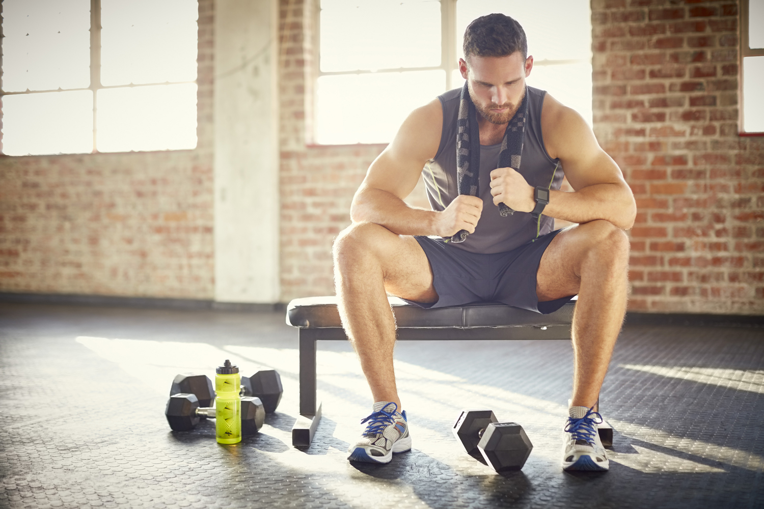 A tired man with towel sitting on a bench in a gym.