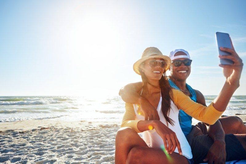 A couple with sunglasses taking a selfie at the beach.