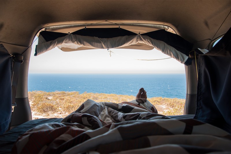 A first-person view of a tired adventurer enjoying the view of the sea from a van.