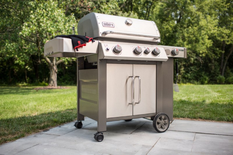 A Weber Genesis II S-335 3-burner propane gas grill on the edge of a patio with lawn in the background.