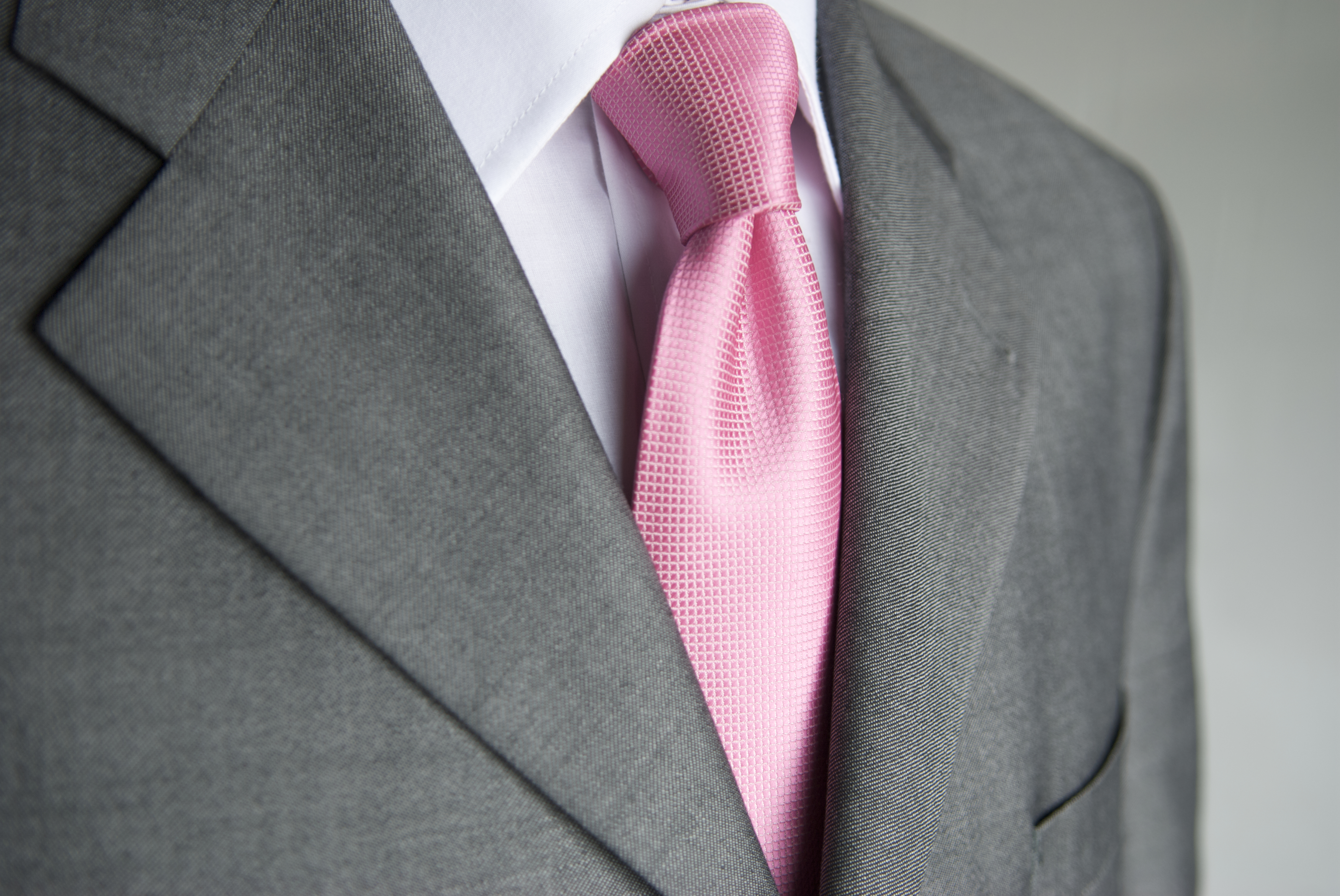 Close-up bright pink necktie makes a colorful contrast to a neutral gray suit on businessman.