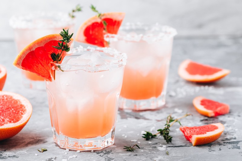 Grapefruit salty dog cocktail with ice in glass on gray stone background