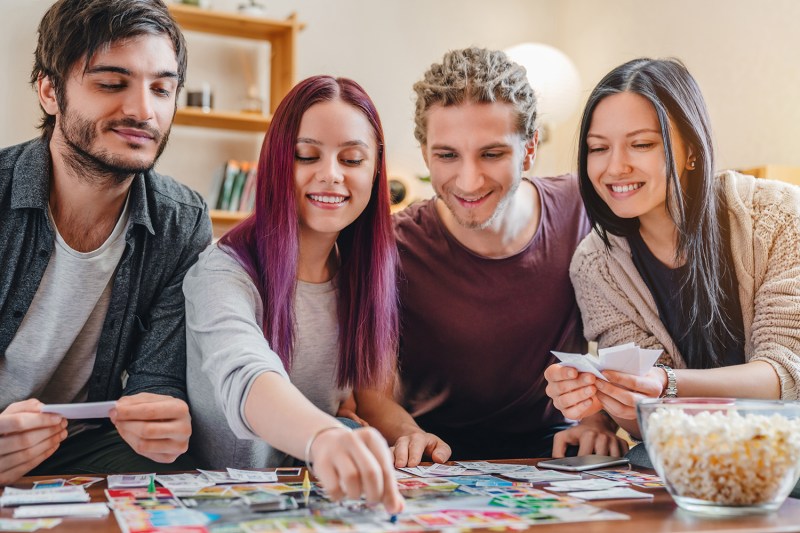 Young group of friends playing board game on table at home interior.