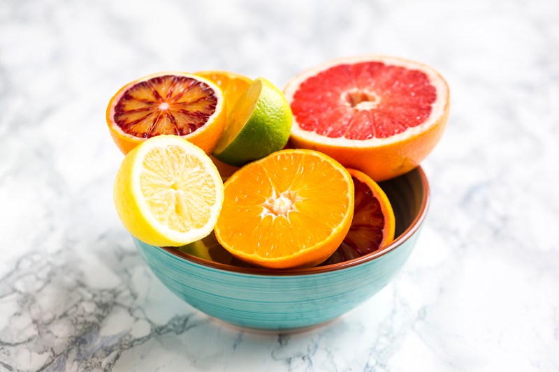 A teal bowl of citrus fruit on marble