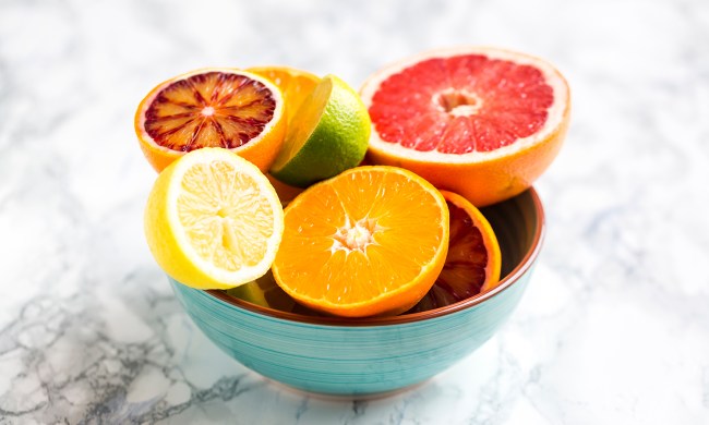 A teal bowl of citrus fruit on marble