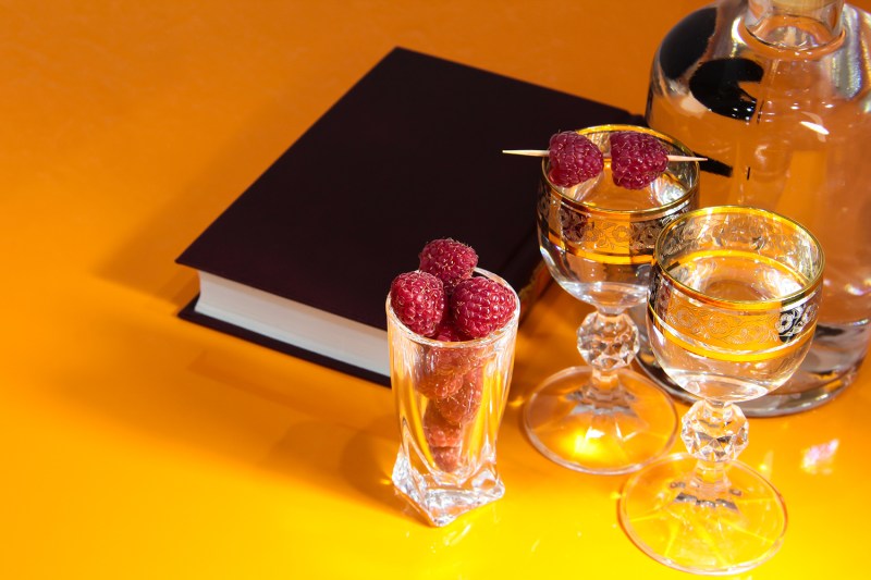 Black book surrounded by cocktail glassware in yellow background.