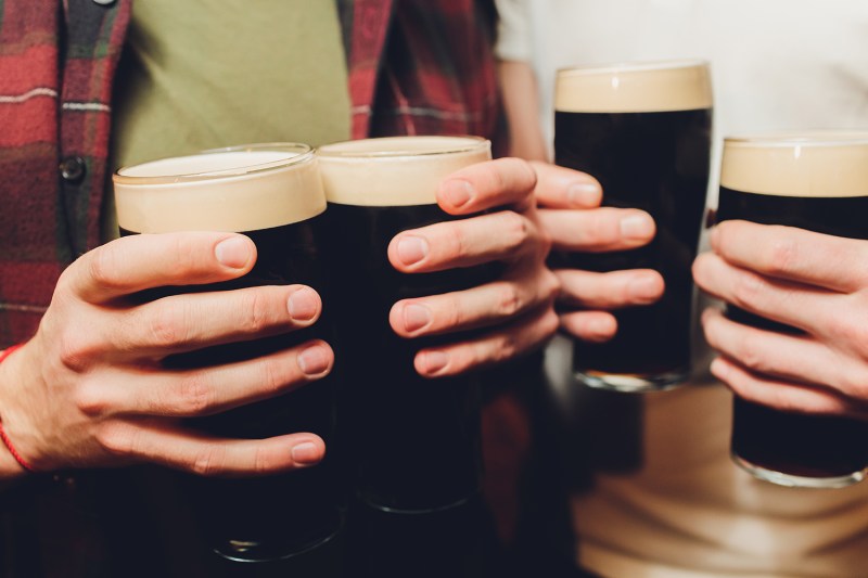 Male group clinking glasses of dark and light beer on brick wall background.