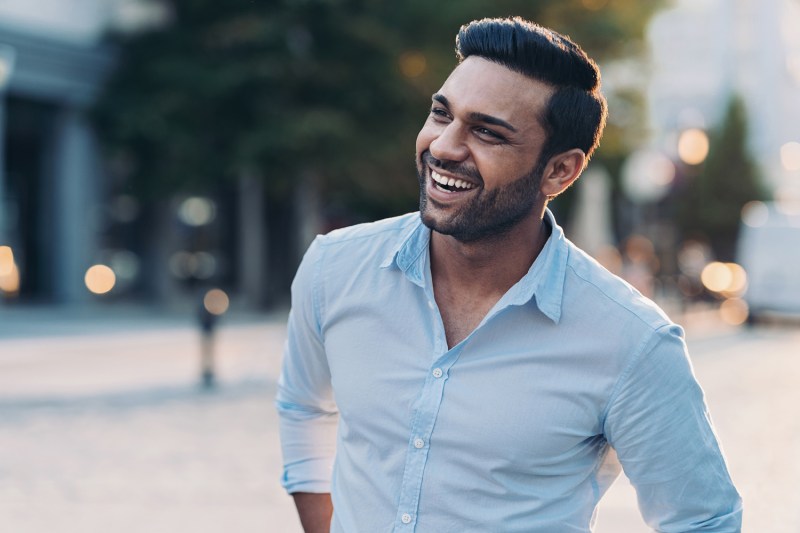 A smiling man wearing a blue shirt in the city.