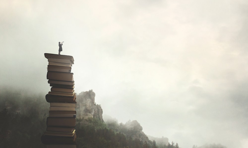 surreal man with telescope looks at infinity from the top of a stack of books in the outdoors.