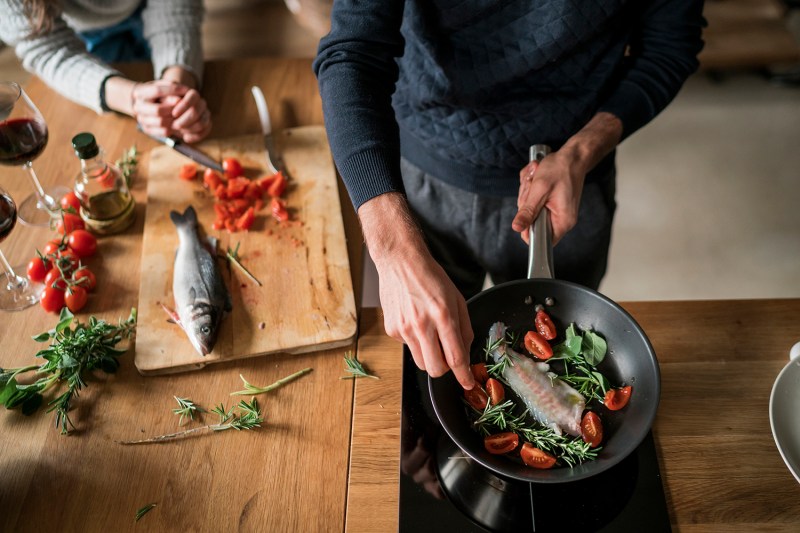 Mid section of young couple preparing fish at kitchen counter.