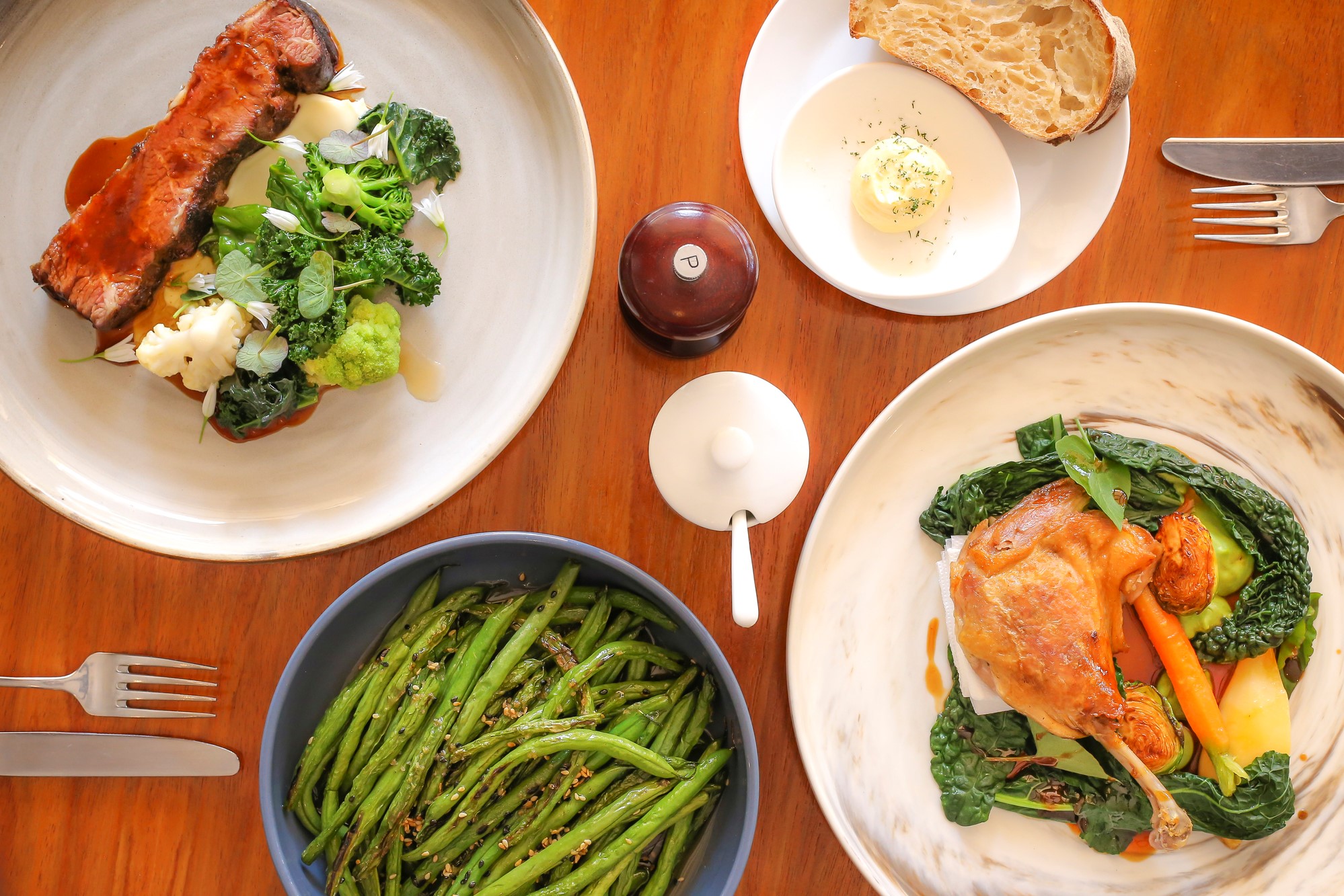 Chicken and steak meals on the table with salt and pepper as well as veggies, green beans, sourdough bread, and butter on the side.