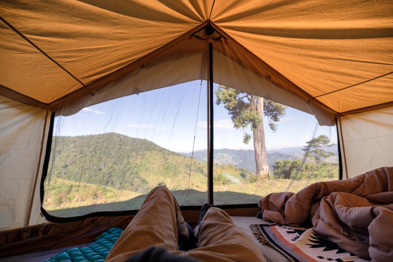 A first-person view of a man relaxing in a tent on a hill.