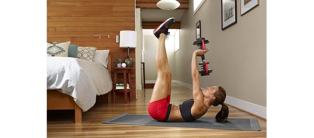A woman in her bedroom performing dumbbell exercises with the Bowflex SelectTech adjustable dumbbells.