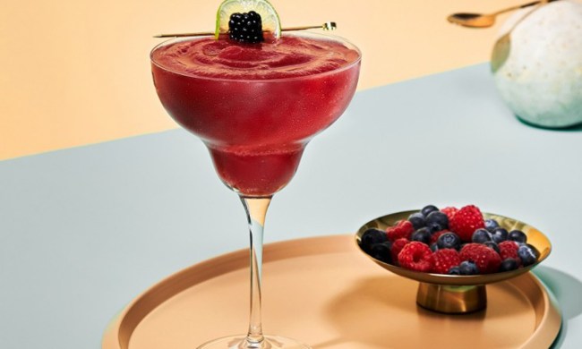A glass of Frozen Berry Margarita beside a bowl of berries on a circular tray.