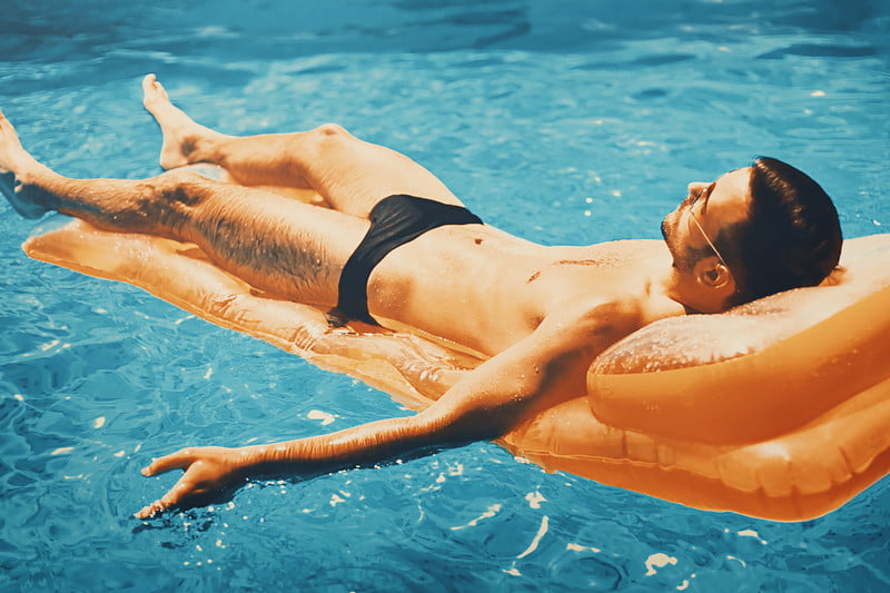 A guy wearing speedo lying on a floaty in a pool.