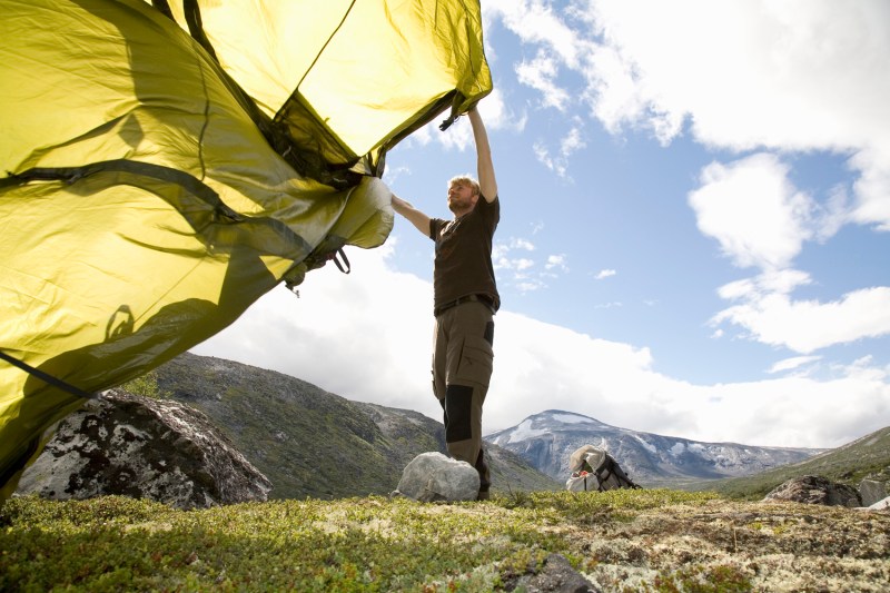 A man preparing to pitch his tent on a mountain.