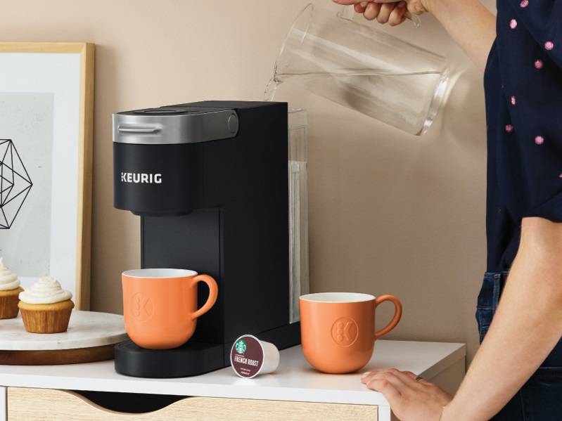 Keurig K-Slim Coffee Maker being filled with water and mugs nearby.