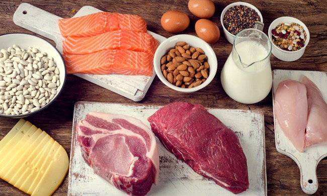 Fish fillets, chicken meat, and red meat on top of distressed white cutting boards along with nuts, cheese, dairy, and eggs.