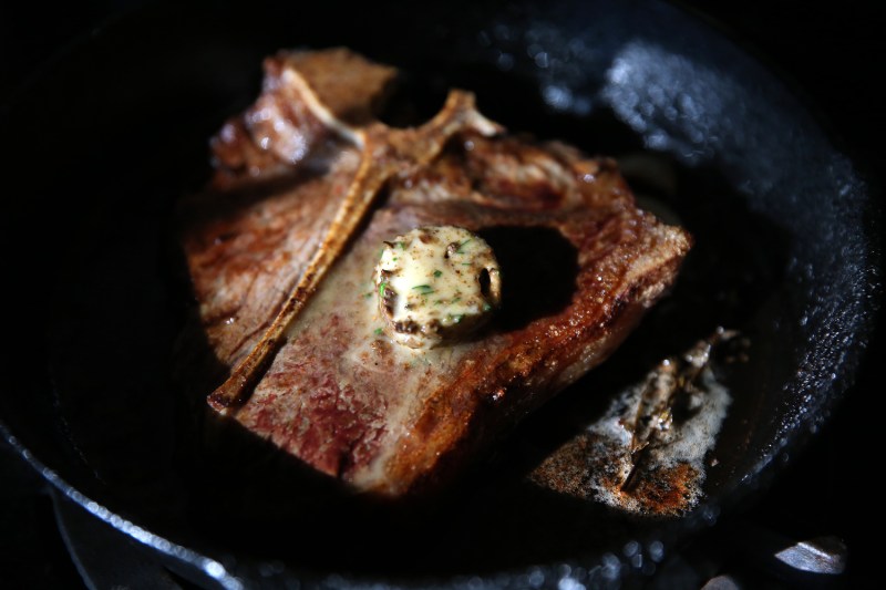 Butter melting on a porterhouse steak in a pan.