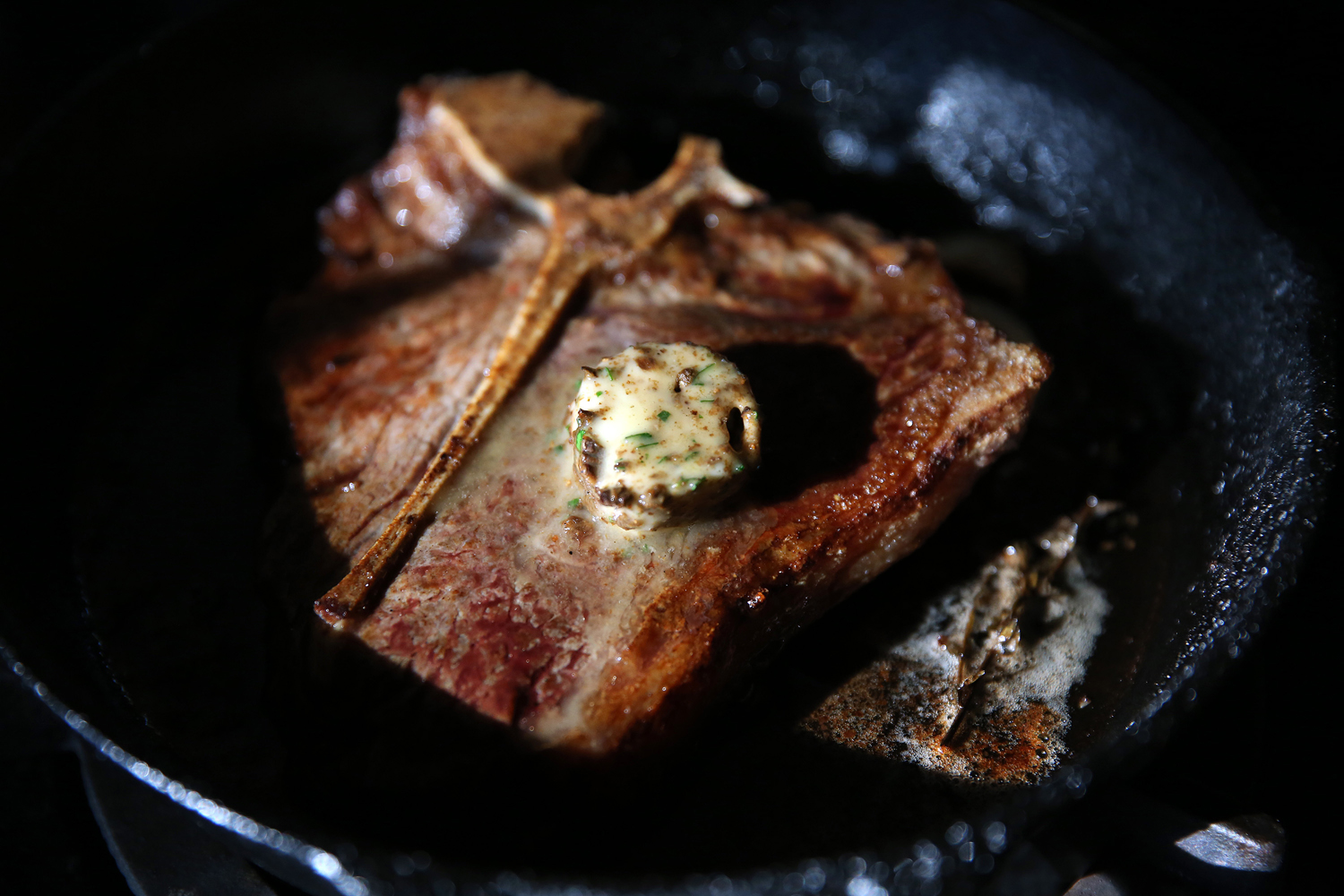Butter melting on a porterhouse steak in a pan. 