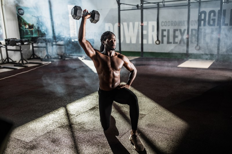 An African-American athlete doing the Single-Arm Reverse Lunge and Overhead Press