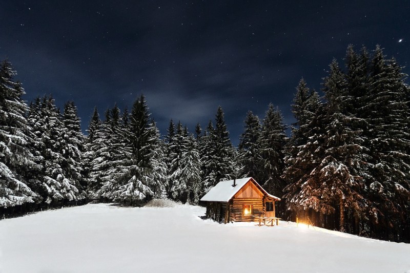 Snowy cabin in the woods at night.