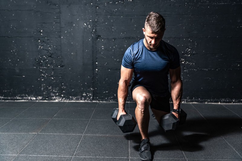 A man uses two dumbbells to perform a split squat.