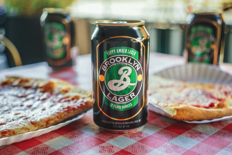 Can of Brooklyn Lager beer in between two slices of pizza.