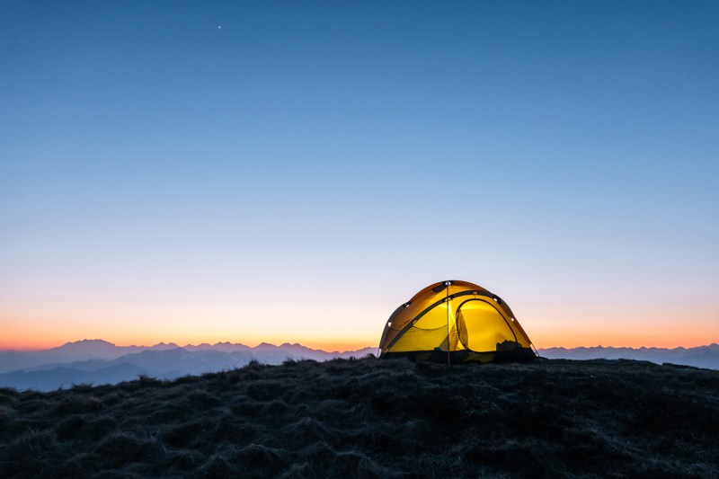 A yellow tent on a mountain ridge at dawn.