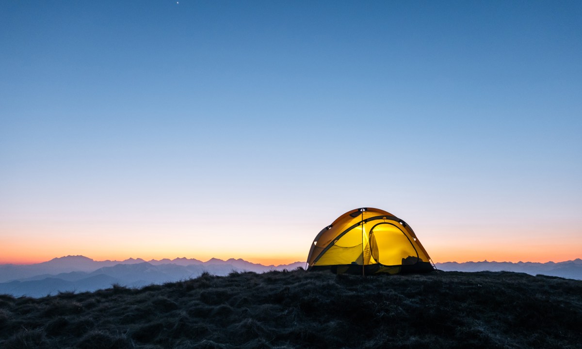 A yellow tent on a mountain ridge at dawn.