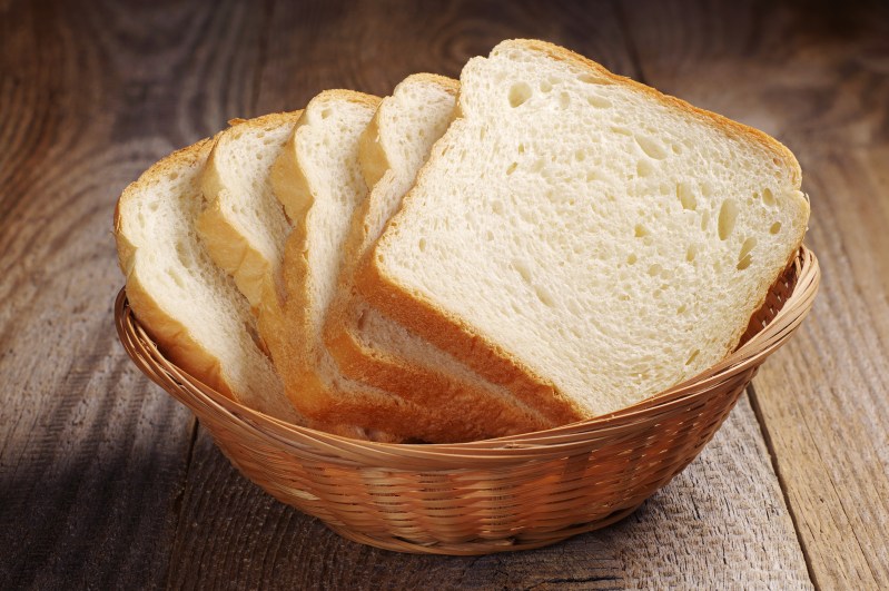 Slices of bread in a wicker basket on a wooden table.