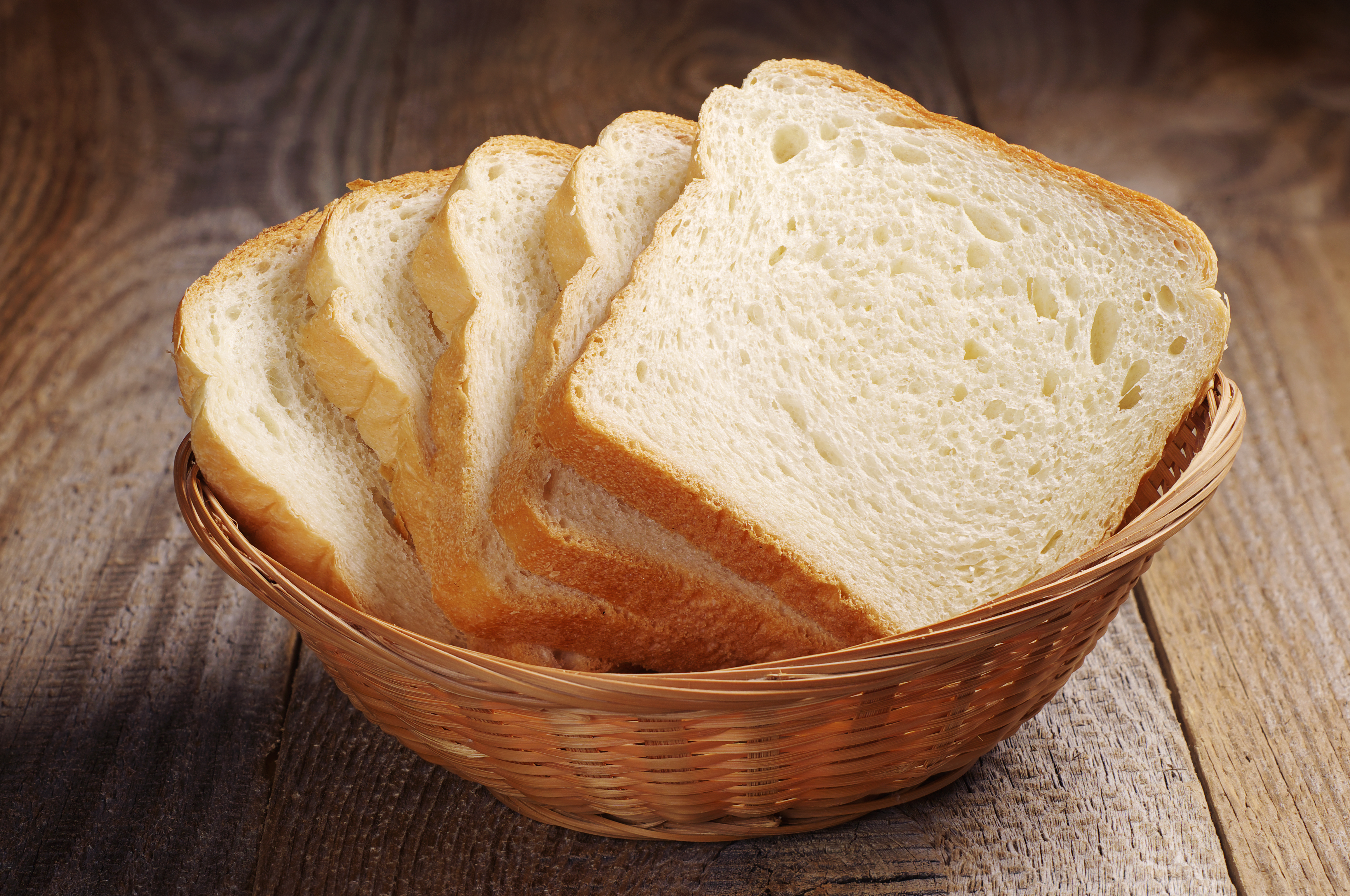 Slices of bread in a wicker basket on a wooden table.
