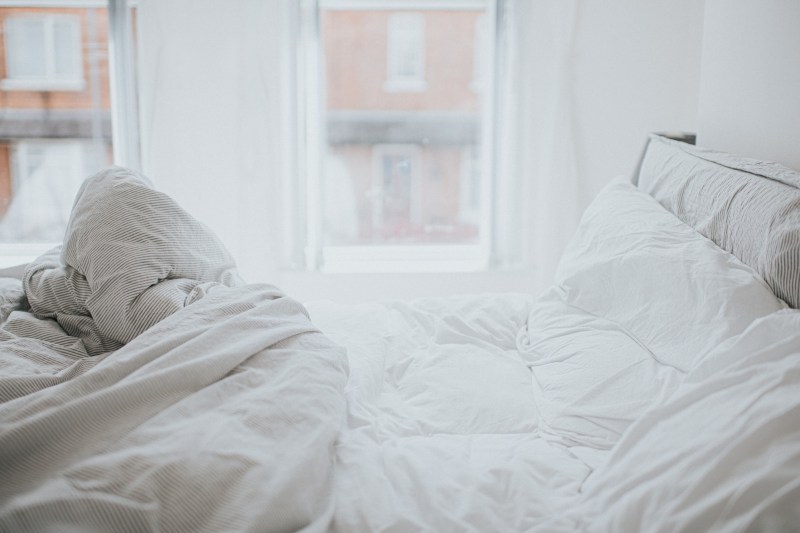 Unmade bed with white blankets and pillows.