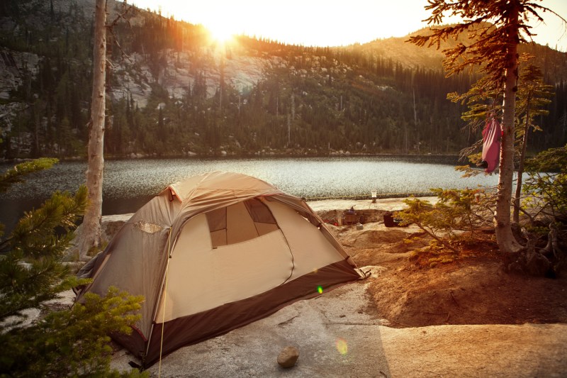 A tent near a body of water with a view of the rising sun.