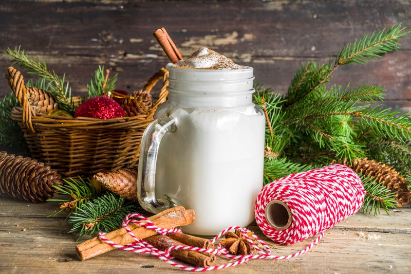 Christmas Tom and Jerry cocktail, whipped cream eggnog with spices, dairy milk beverage, with christmas decorations, rustic wooden background copy space.