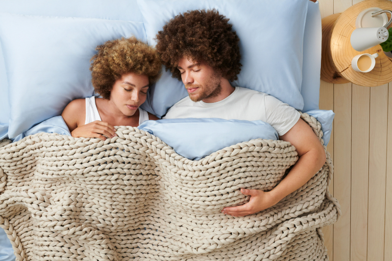 A couple snuggles under Bearaby's weighted, fall-colored blanket