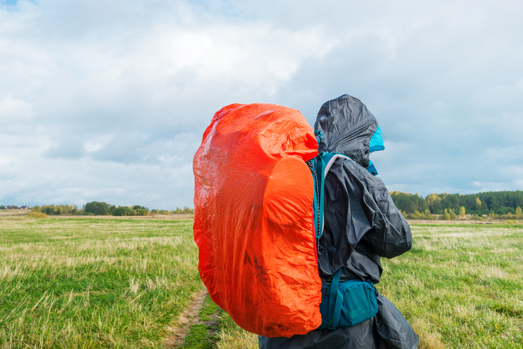 Man hiking with bright red backpack on a green field.