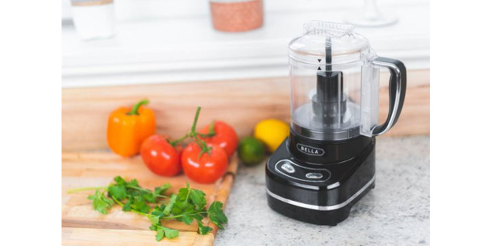 Bella 3-Cup Mini Chopper on a kitchen countertop surrounded by vegetables.