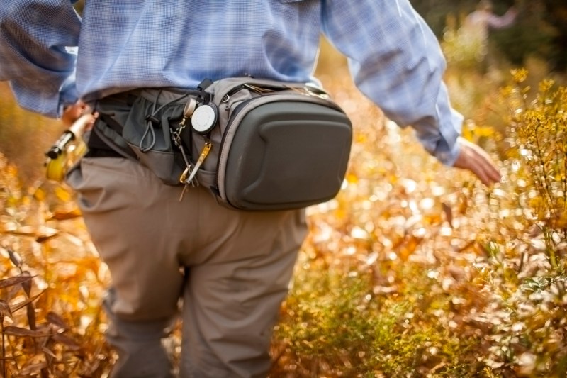 A rear view of a man with a waist pack walking in a field. 