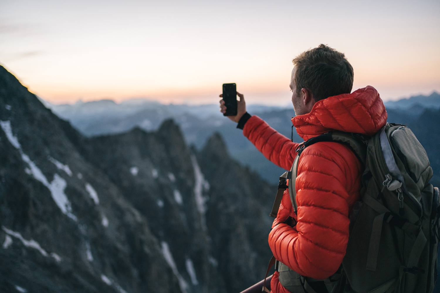 A hiker in puffer jacket taking a picture of the mountain view.