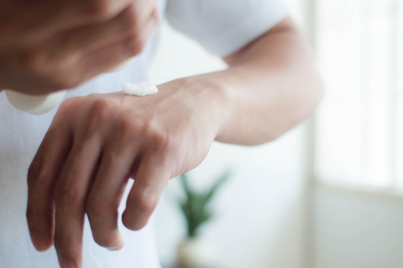 A close-up view of a man applying lotion to his hands.