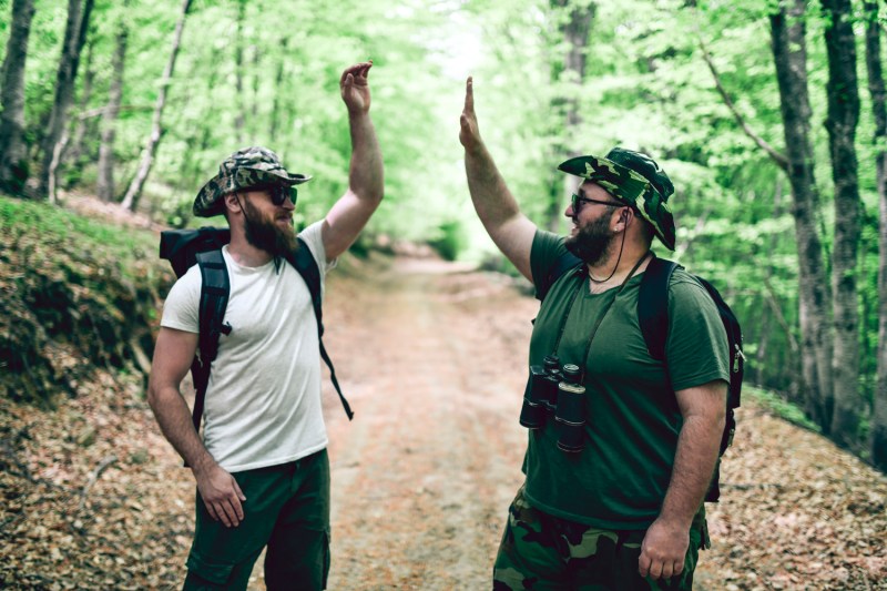 Two male hikers making a high five in a forest.